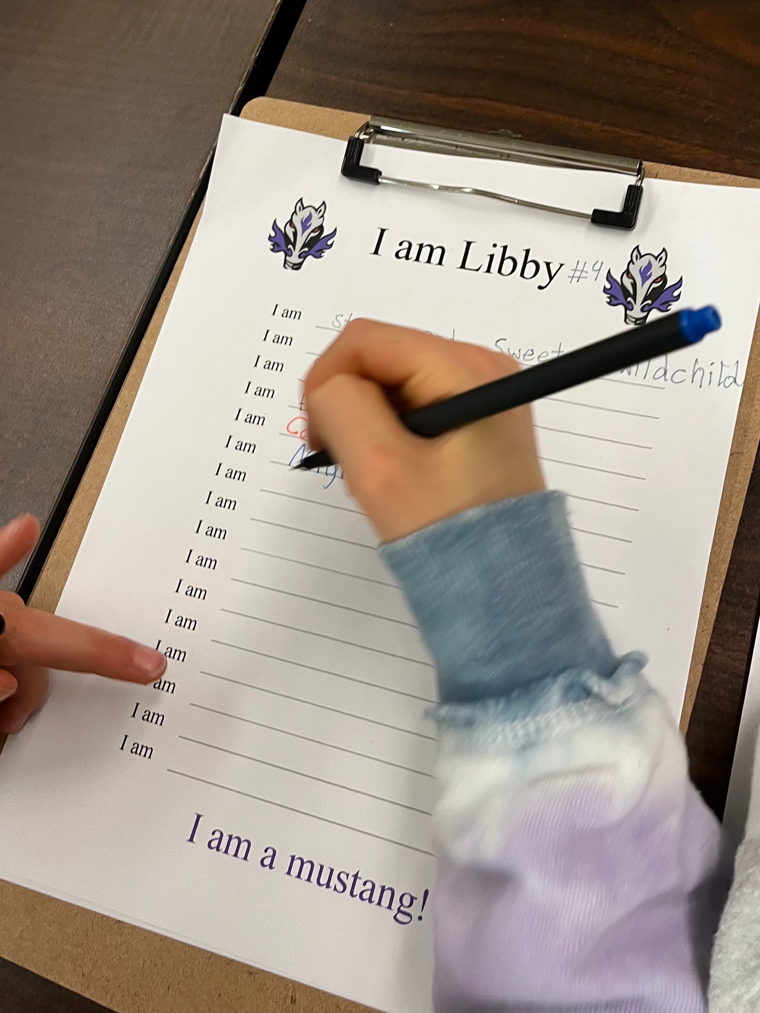 Person writing on a sheet labeled 'I am Libby' with a pen, held over a clipboard.