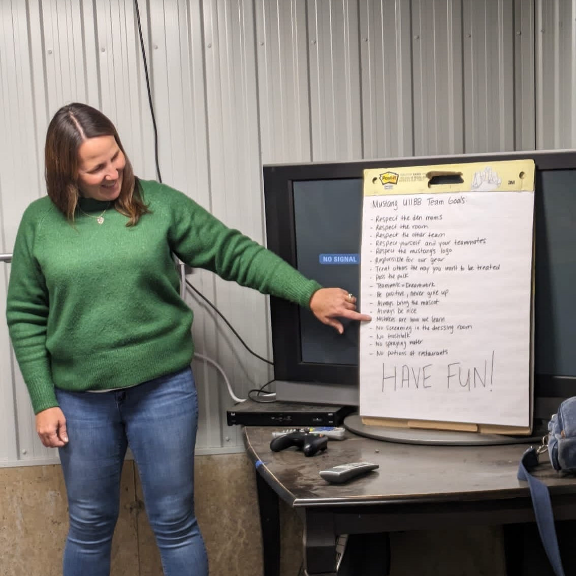 Sarah Kinlin in green sweater pointing at a whiteboard with text.
